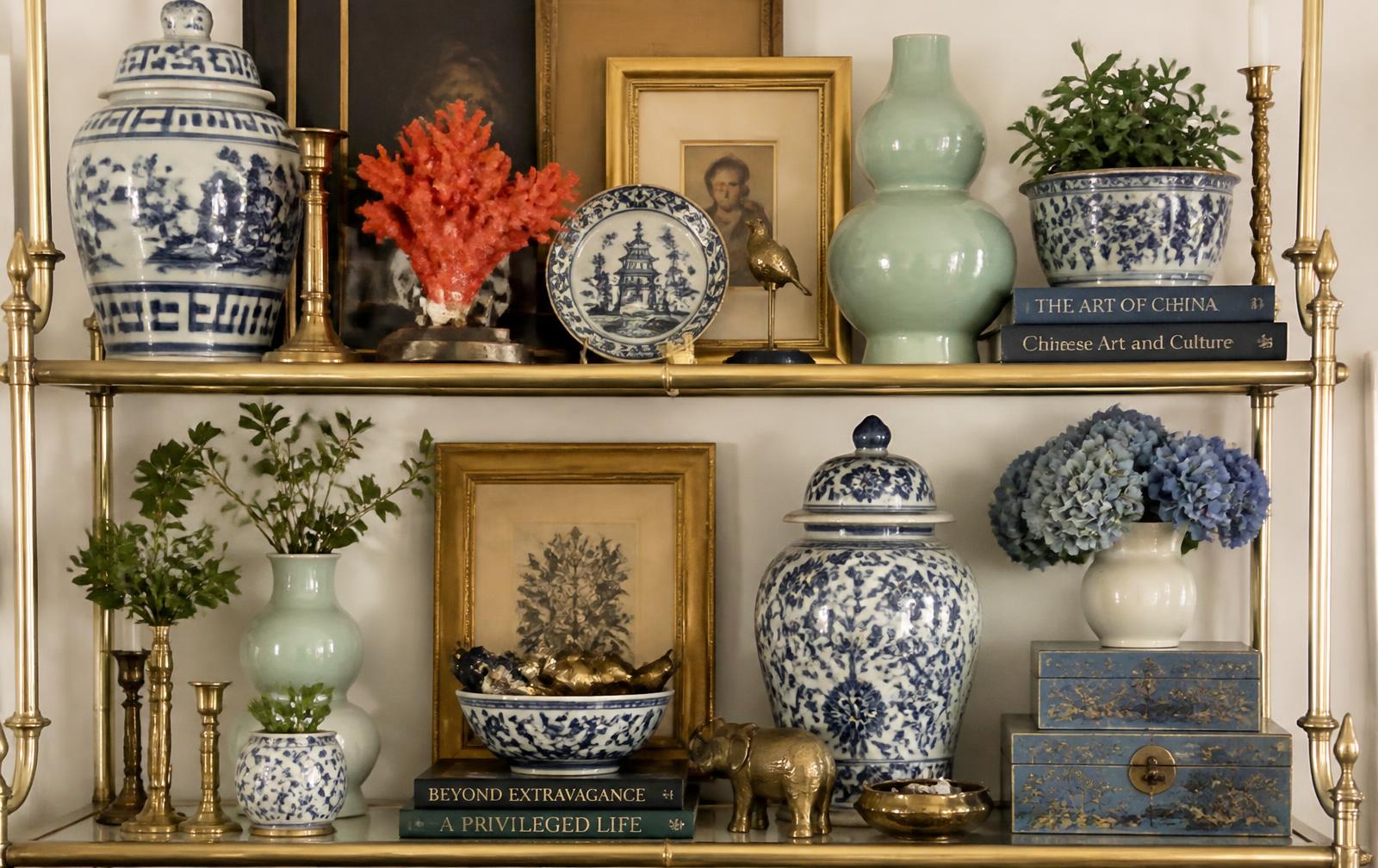 Brass shelves layered with blue and white porcelain, celadon vases, coral and gilt frames