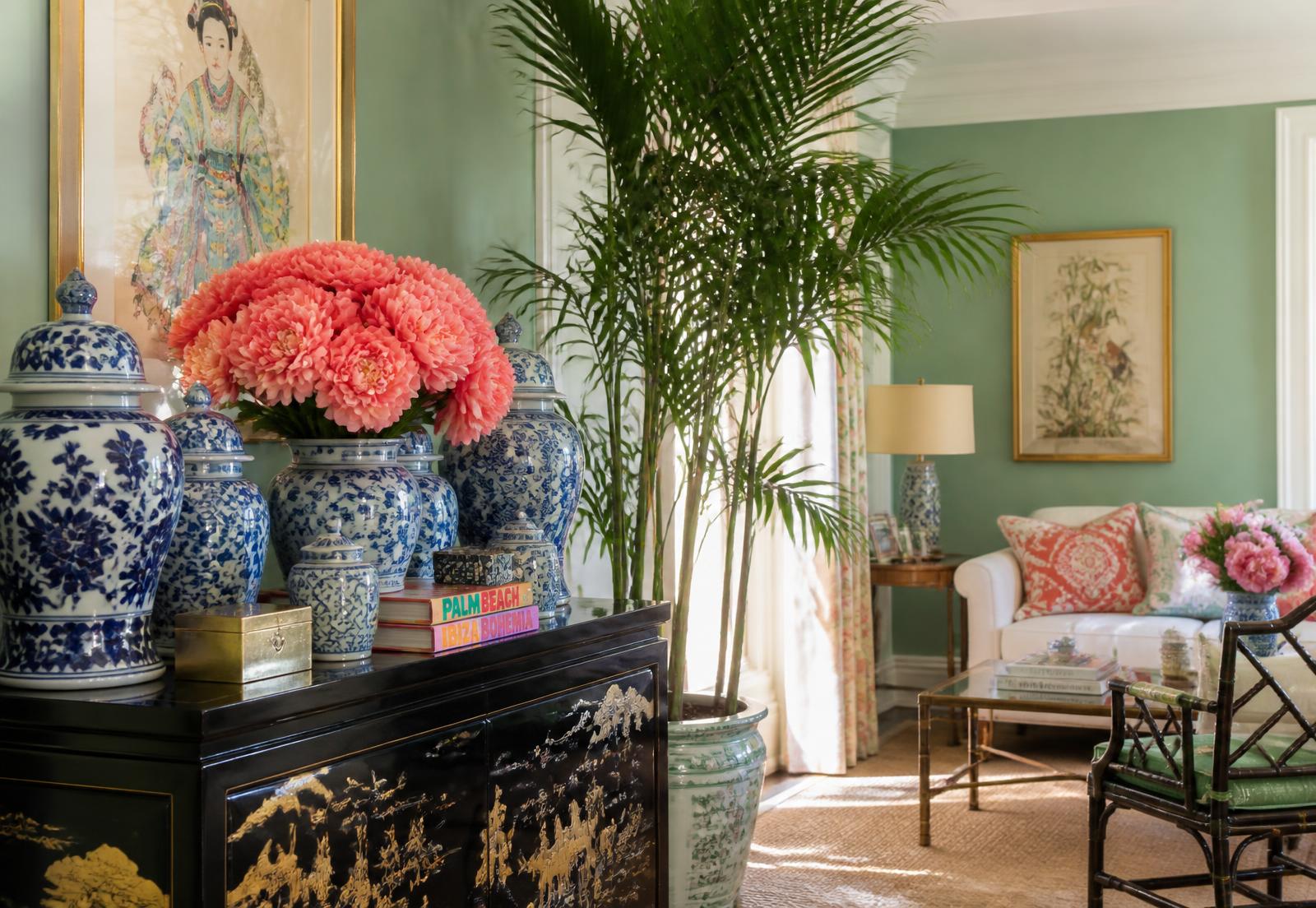 Celadon green sitting room layered with blue and white ginger jars, coral peonies and a palm